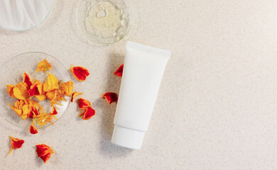  Still life composition with  cosmetic tube for face, eyes, hand cream or body lotion on a light background with medical glasses and flower petals, oil and cream texture. Autumn beauty care.