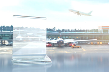 Blank transparent table sign against the background of the airport with standing planes. Template for information on travel and flights. Background with blank sign on pandemic theme.