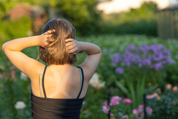 Naklejka na ściany i meble Back view of a girl with beautiful hair admiring a blooming evening summer garden