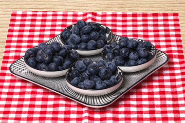 Closeup of a decorative plate with four bowls with fresh blueberries on a rustic wooden table with red napkin. Concept of healthy nutrition. Space for your design.
