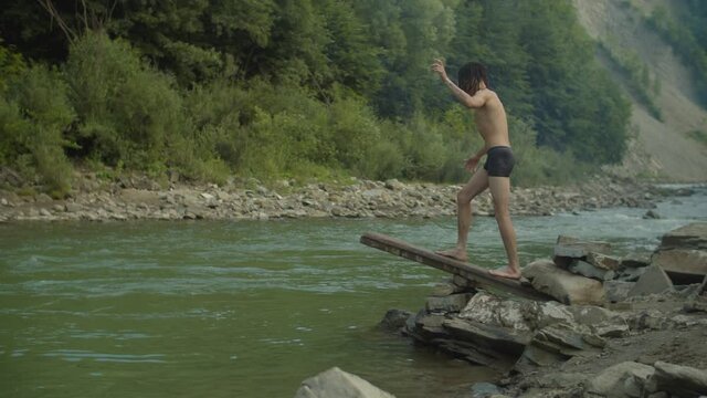 Carefree handsome arab man diving into mountain river off handmade wooden springboard while positive guy having fun, enjoying recreation and swimming during summer vacations in mountains.
