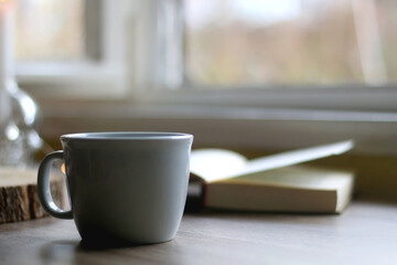 Bowl of cookies, cup of hot beverage, open book and lit candles on a table. Selective focus.