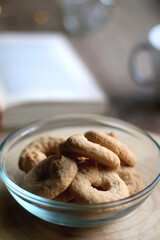 Bowl of cookies, cup of hot beverage, open book and lit candles on a table. Selective focus.
