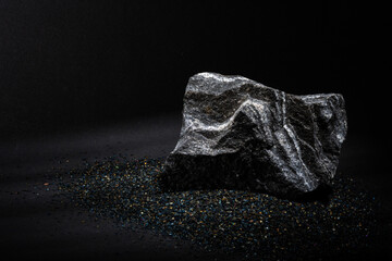 A stone, a piece of hard rock of a natural gray color of an angular shape on a dark background and with streaks of light on the surface