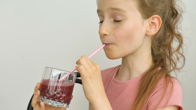 Sweet little girl drinks raspberry smoothie and smiles. Vegetarian drink. Close-up portrait of a child who enjoys a refreshing tasty raspberry juice, healthy eating