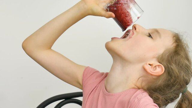 Sweet little girl drinks raspberry smoothie and smiles. Vegetarian drink. Close-up portrait of a child who enjoys a refreshing tasty raspberry juice, healthy eating