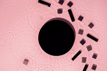 Abstract black geometric figures composition on transparent pink clear calm water texture with splashes. Flat lay cosmetic mockup podium for product presentation. Water waves in sunlight, copy space.