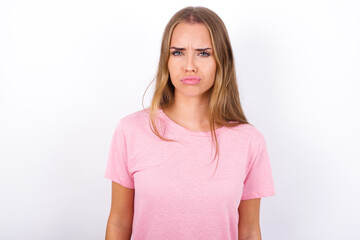 Offended dissatisfied beautiful blonde girl wearing pink t-shirt on white background with moody displeased expression at camera being disappointed by something