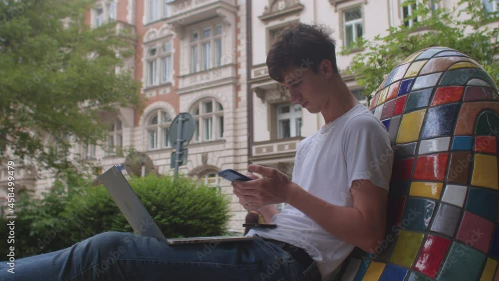 Poster a young man uses the phone on the street of the courtyard of the house. hands typing text on the key