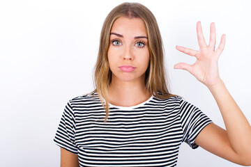 beautiful blonde girl wearing striped t-shirt on white background purses lip and gestures with...