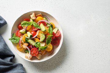 Tuscan summer Panzanella with tomatoes, crispy bread, red onion on white background with copy space. Top view. Italian cuisine. Mediterranean healthy food. Summer vegetables colorful salad.