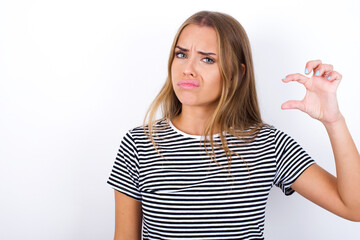 Displeased beautiful blonde girl wearing striped t-shirt on white background shapes little hand...