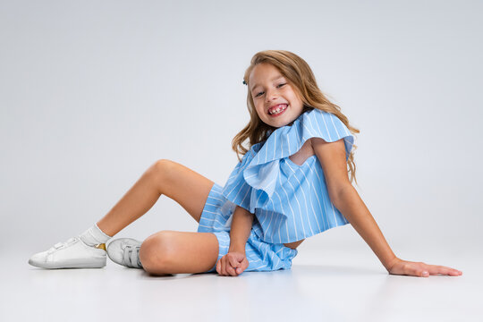 Beautiful little girl in blue holiday outfit sitting on floor isolated on white studio background. Happy childhood concept. Sunny child.