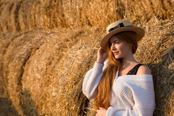 Naklejka na ściany i meble Portrait of a beautiful happy girl in a hat on a background of hay. 