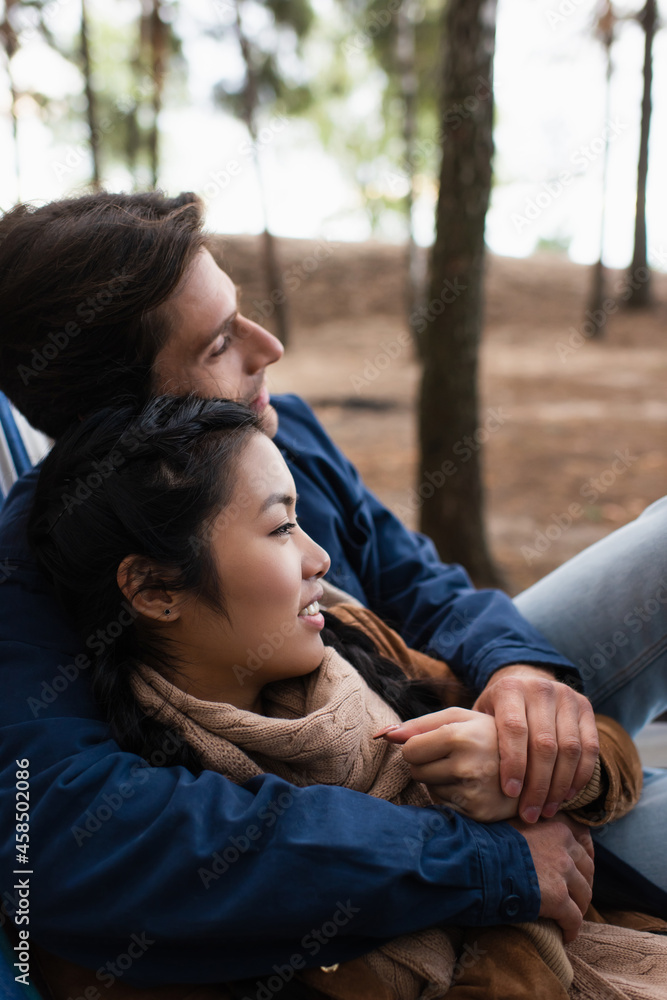 Wall mural side view of interracial couple smiling while hugging in hammock