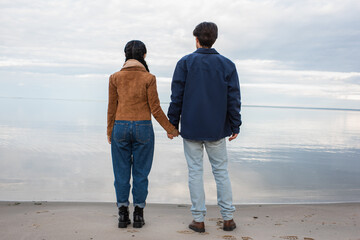 Back view of couple holding hands on shore near sea