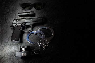 Black gun, flashlight, glasses, camera and Police metal real handcuffs lie on the black background....