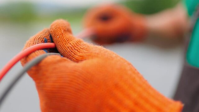 An electrician worker holds a red and black high-voltage electric cable, checks the quality of the cables. Connecting electrical cables. Close up of male hands in protective gloves holding cable
