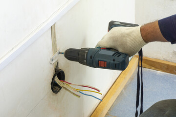 The electrician makes an electrical outlet, electrical wires stick out of the wall, the man's hand...