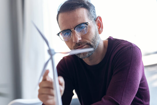 Handsome business man working on new alternative energy development looking at a model of a wind turbine in modern startup.