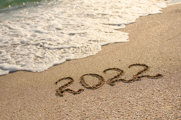 Sandy beach, sea wave and the inscription 2022. New Year 2022 Concept