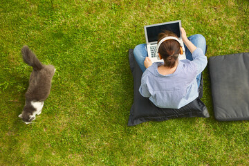Woman with laptop computer and cat from above in the garden