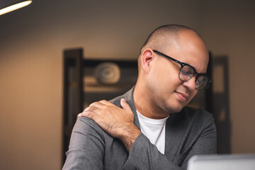 Young businessman works late at night in a dimly lit room. He tired and stressed needs rest. He has...