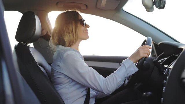 Happy caucasian woman with blond hair enjoying driving car alone. Business lady wearing sunglasses and formal clothes. Vehicle and people concept.
