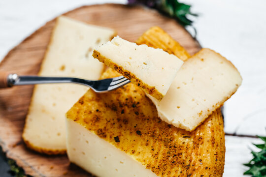 Cheese pieces of hard yellow Dutch gouda cheese with dried spices on wooden board
