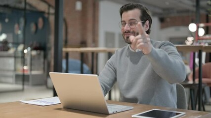 Young Man Pointing at Camera while using Laptop in Office