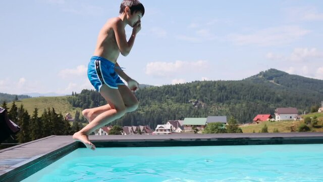 Happy boy jumping into swimming pool against forest mountain and sky