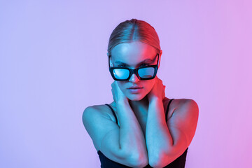 Young woman touching her sunglasses on pink neon light background.