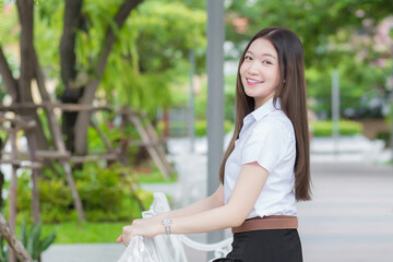 Portrait of an adult Thai student in university student uniform. Asian beautiful girl sitting smiling happily at university with a background of garden trees.