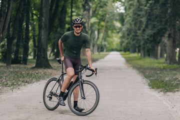 Fototapeta premium Smiling cyclist in sport clothes posing with bike at park