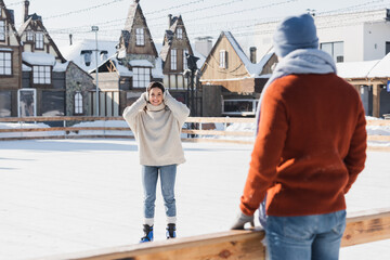 smiling young woman in ice skates looking at blurred boyfriend on foreground