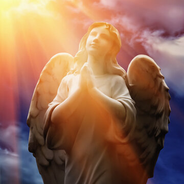 Beautiful angel with wings looking up at the sky in rays of light. Ancient statue.