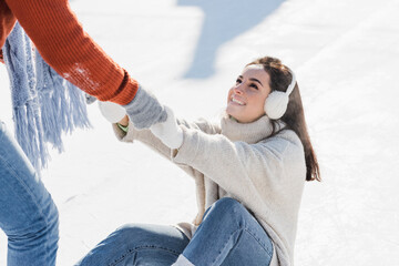 man in gloves helping smiling girlfriend get up on ice rink