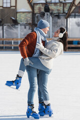 full length of cheerful man lifting leg of happy girlfriend on ice rink