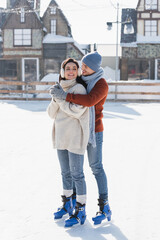 full length of happy man hugging young woman in ear muffs on ice rink