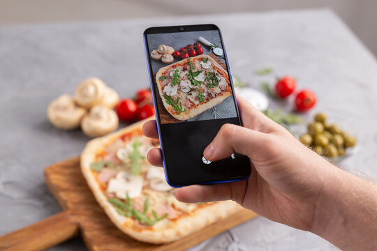 Smartphone shot food. Italian traditional pizza with cheese, ham and mushrooms. Social networks and delivery food application concept.