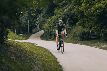 Male athlete riding black bike on among green city park