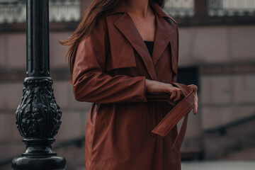 Cropped stylish young woman in fashionable long brown leather coat. Pretty elegant girl model...