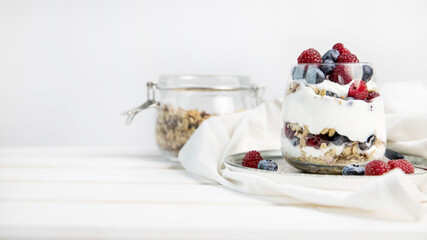 Granola parfait with berries and yogurt with a copy space.  Parfait with granola , raspberries and blueberries on a white background with copy space. Granola in a glass . 