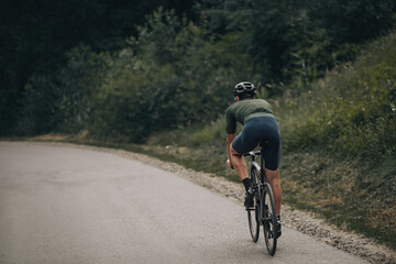 Fototapeta na wymiar Back view of male athlete riding bike at green park