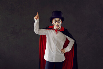 Child in vampire costume against dark studio background. Kid dressed as Dracula for Halloween...