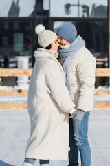 young couple in winter hats holding hands while kissing outside