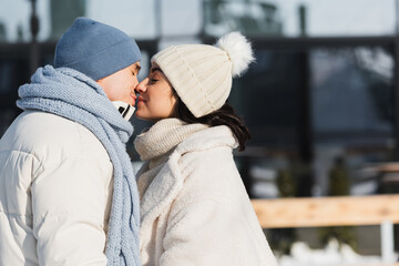 young couple in winter hats kissing outside