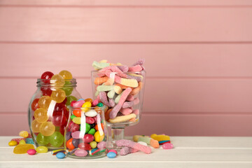 Jars with different delicious candies on white wooden table against pink background, space for text