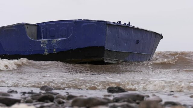 Blue metal boat swaying on the waves near the shore. Windy autumn weather on the shore of Lake Ilmen.