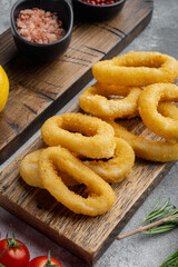 Crunchy deep fried squid or onion rings in batter, on serving board, on gray stone table background